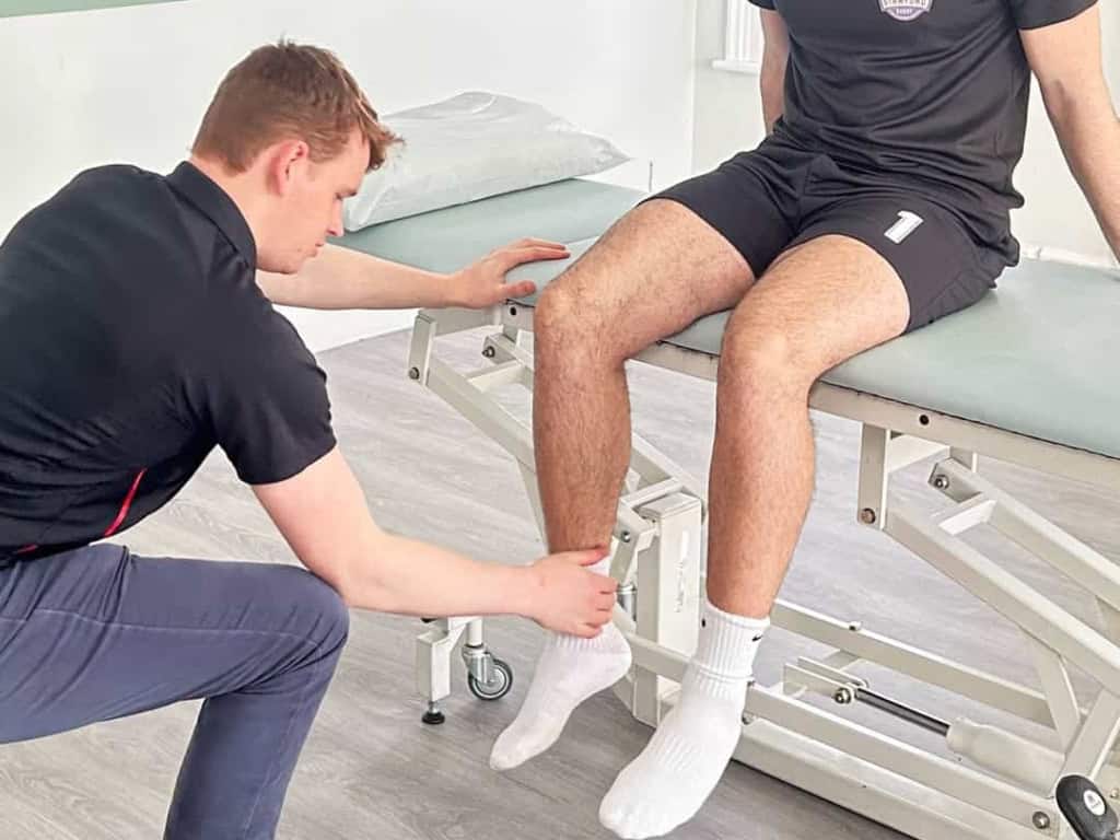 Physiotherapist examining a seated patient's ankle and foot