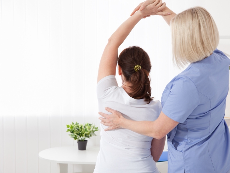 Clinician supporting a woman's arm through a shoulder stretch