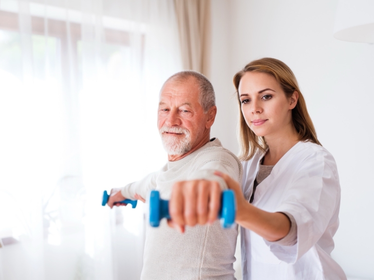 Clinician coaching an older man through an arm exercise with hand weights