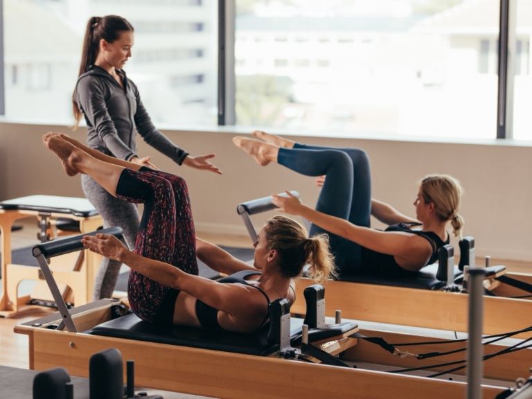 Pilates instructor guiding a small class on studio equipment