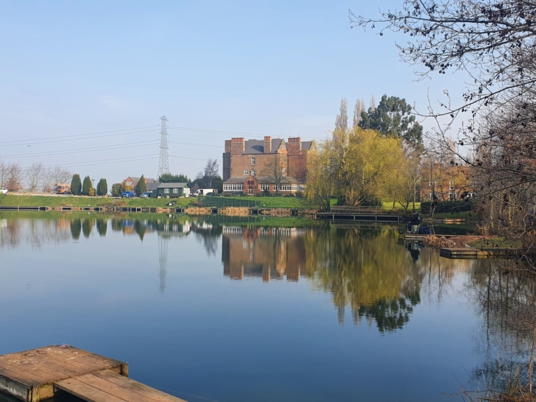Trees and buildings reflected in a still lake on a spring morning