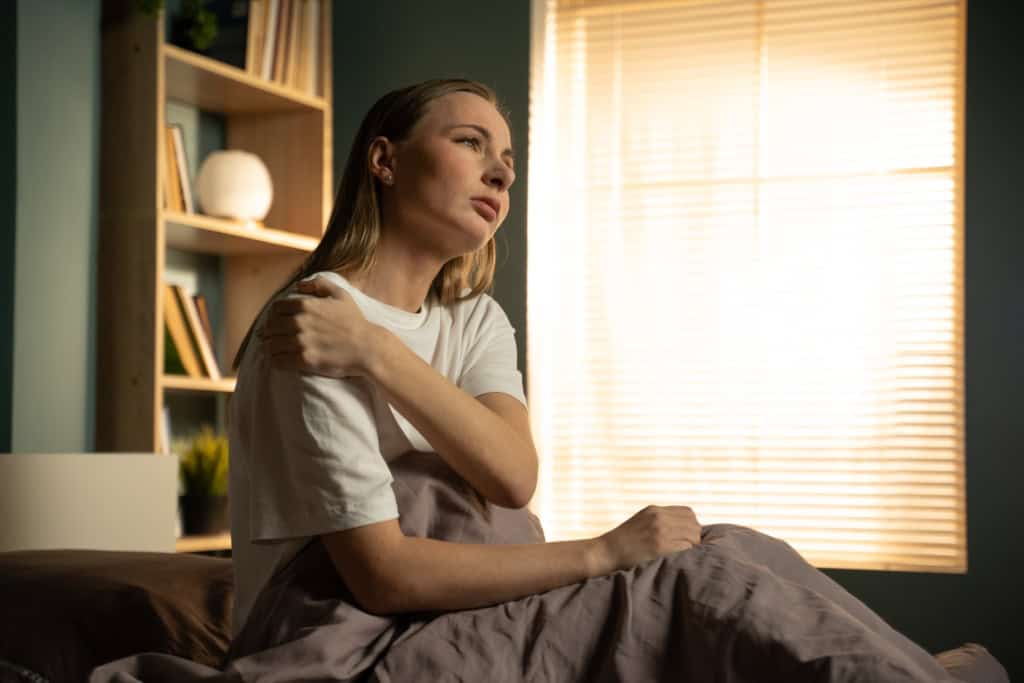 Woman sitting up in bed holding her painful shoulder